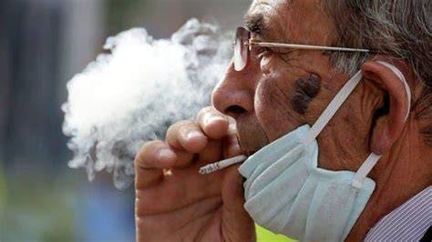 Persona fumando con mascarilla bajada en calle